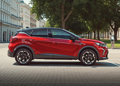 Roter Mitsubishi ASX Select in schräger Heckansicht fährt durch eine breite Stadtstraße mit Häuserfassaden und Cafés im Hintergrund – betont das dynamische Design des kompakten SUV im urbanen Umfeld.