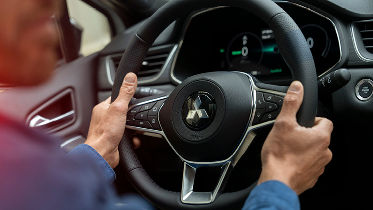 Nahaufnahme eines Fahrers, der das Multifunktionslenkrad des Grandis Select mit beiden Händen hält; im Hintergrund sind digitale Instrumente und Bedienelemente des Cockpits zu sehen.