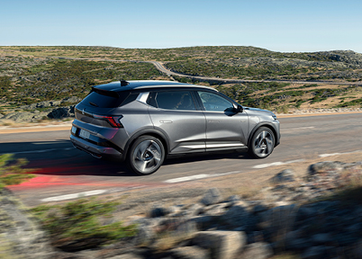 Graue Eclipse Cross Intro Edition in schräger Heck-Seitenansicht fährt dynamisch auf einer kurvenreichen Landstraße durch eine karge Hügellandschaft bei blauem Himmel – unterstreicht den sportlich-elektrischen Auftritt des E‑SUV.