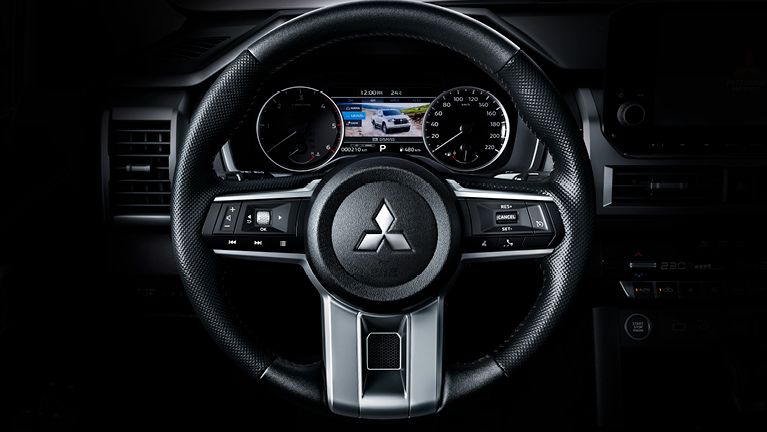 Frontale Nahaufnahme des Mitsubishi L200 Cockpits mit beleuchtetem Multifunktionslenkrad, analogen Rundinstrumenten und zentralem Farbdisplay im Kombiinstrument – vermittelt Übersichtlichkeit und robuste Funktionalität im Fahrerbereich.