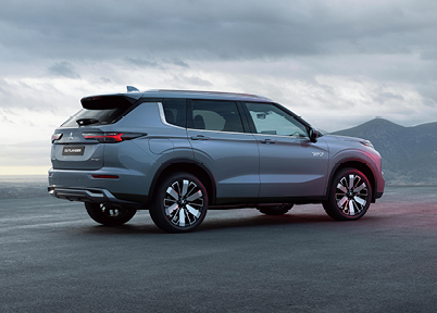 Seitliche Rückansicht eines grauen Outlander Plug-in Hybrid Select, der auf einer leeren Bergstraße steht; im Hintergrund ein bewölkter Himmel und angedeutete Berge.