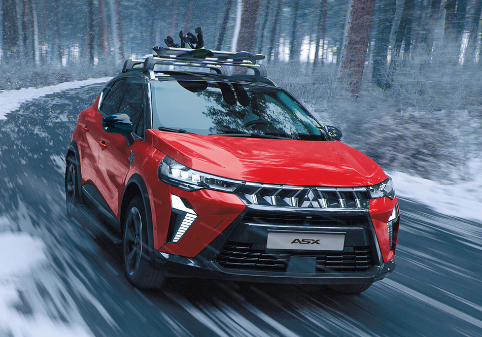 Roter Mitsubishi ASX SUV mit Dachgepäckträger fährt dynamisch durch eine verschneite Kurve im Wald.