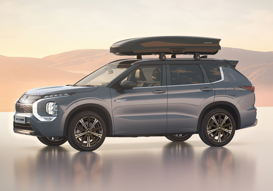 Seitenansicht eines grauen Outlander Plug-in Hybrid Select mit montierter Dachbox, der auf einer glänzenden Fläche vor einer sanften Berglandschaft im warmen Licht des Sonnenuntergangs steht.