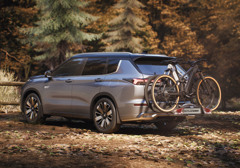 Silberner Mitsubishi Outlander Plug-in Hybrid steht am Waldrand, auf der Anhängerkupplung sind zwei Fahrräder montiert, am Boden liegt herabgefallenes Herbstlaub.